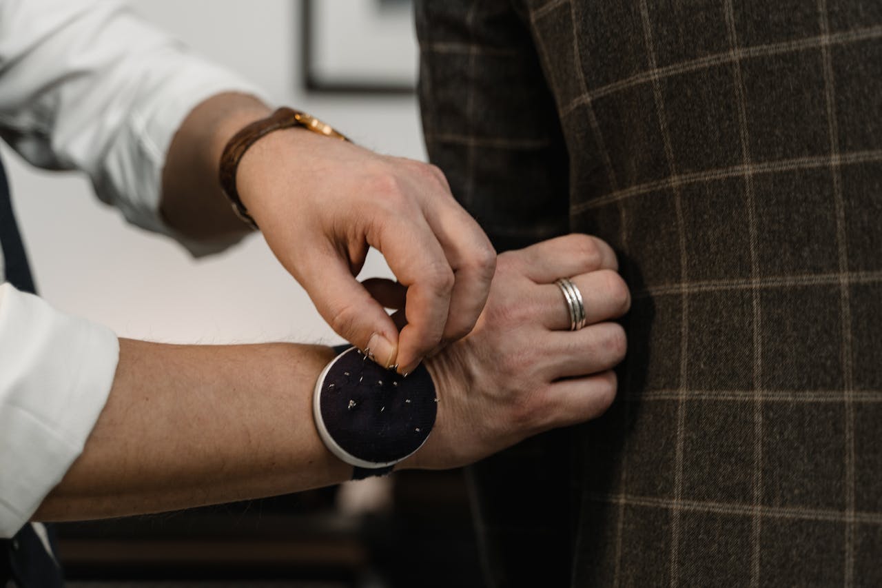 Home Close-up of a tailor adjusting a checkered suit jacket during a fitting session.